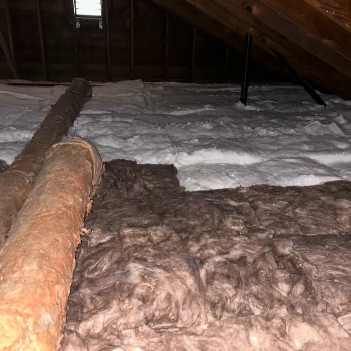 Attic with old brown insulation partly cleared and fresh white insulation laid down