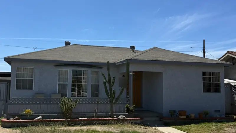 Gray stucco house with an older roof and a tall cactus out front