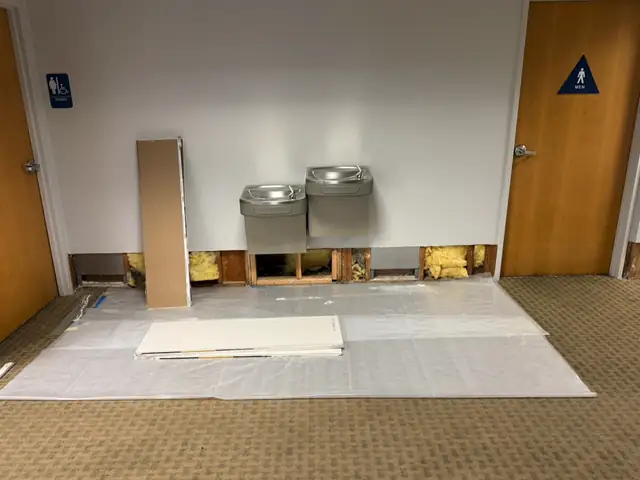 Water-damaged wall with drywall cut out and removed in a commercial office